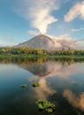 平静的湖水中倒映着美丽的火山日出景色，四周环绕着郁郁葱葱的绿色植物