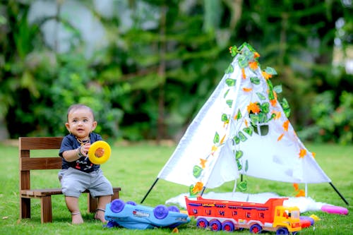 Boy Sitting on a Chair Surrounded by his Toys on the Lawn 