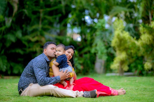 Family with a Baby Boy Sitting and Posing on a Lawn 