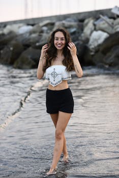 Smiling woman walks on the beach, adjusting her hair at sunset. Perfect for lifestyle and travel themes.