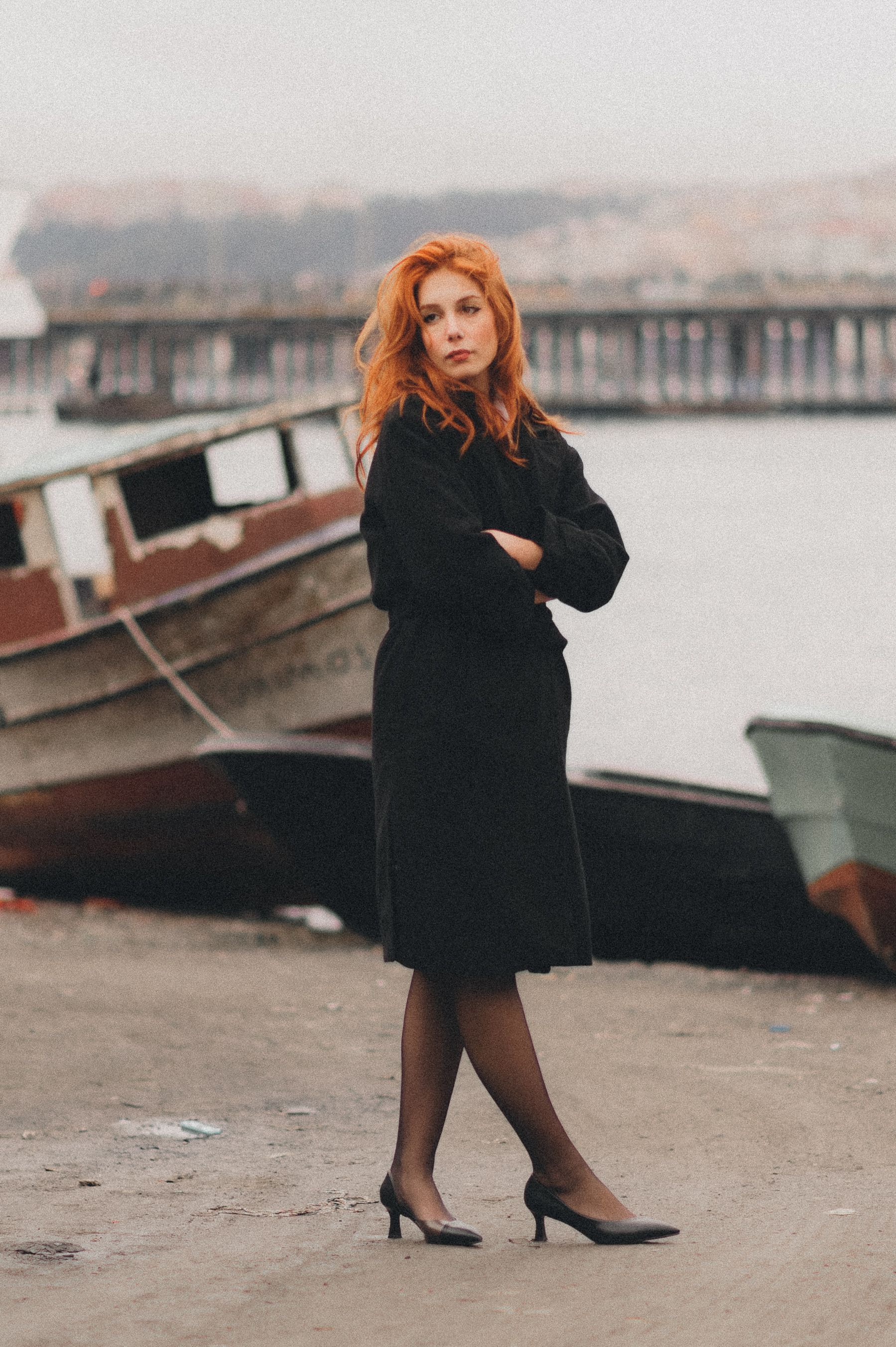 A fashionable woman poses by the harbor in İstanbul, Türkiye, wearing a chic black dress.