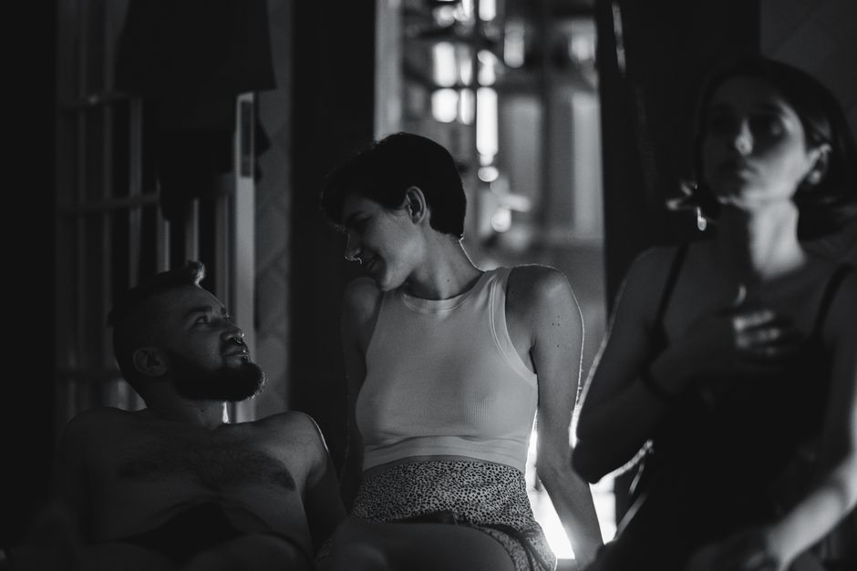 A candid black and white photo of three young adults enjoying an intimate indoor moment.