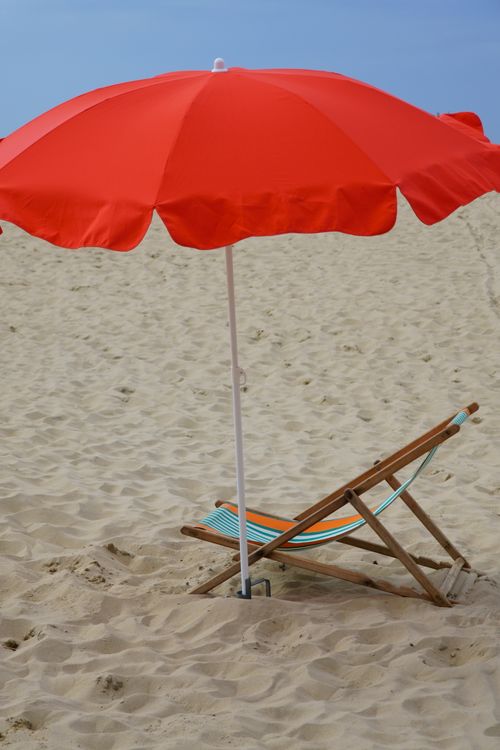 Free Bright red umbrella and deckchair on a sandy beach under clear skies. Stock Photo