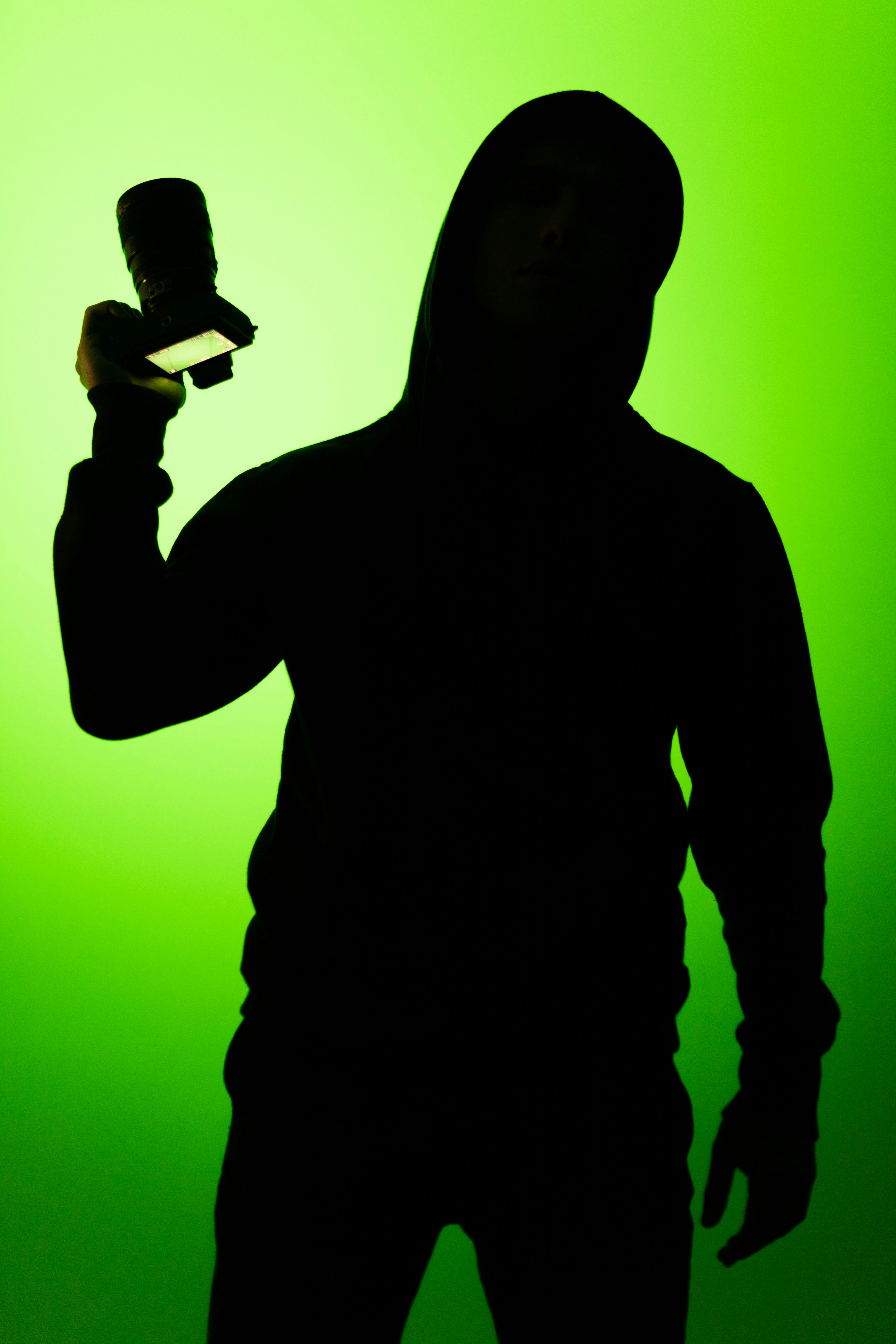 Silhouette of a person holding a camera against a vibrant green background.