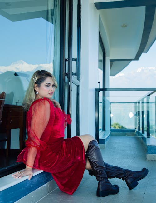 Woman in Burgundy Red Dress and High Boots Posing on a Balcony