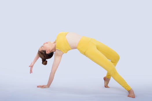 Athletic woman in yellow sportswear posing gracefully in an acrobatic move on a white background.