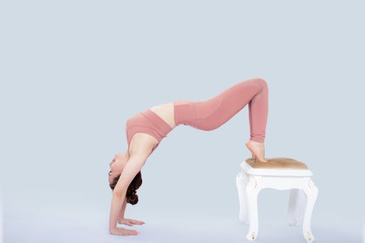 Woman in sportswear doing a yoga backbend pose on a white stool in studio.