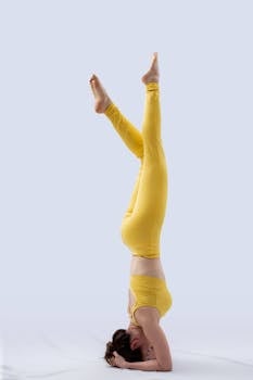 Young woman performing a headstand in a yellow outfit in a studio setting.