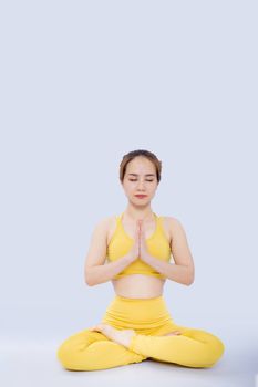 Woman meditating indoors in a yellow yoga outfit against a plain background.