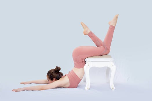 Young woman in pink sportswear performing a yoga pose on a white stool.