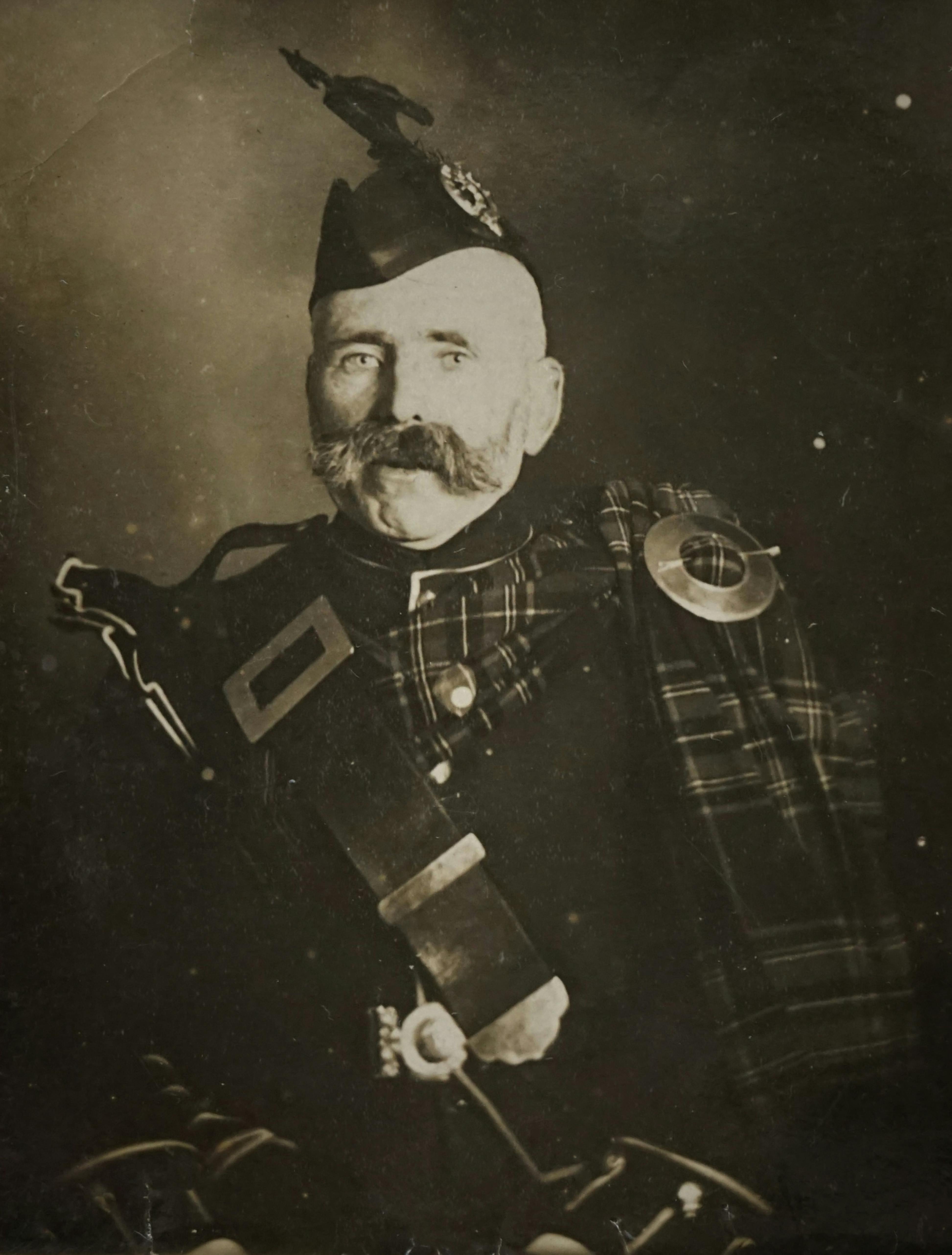 A vintage portrait of a Scottish soldier wearing traditional tartan uniform with a distinctive mustache.