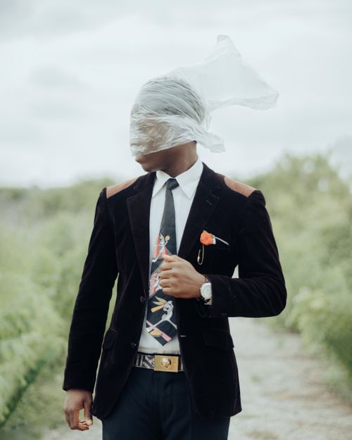 Free A man in a suit with a creative twist wearing a plastic bag headpiece, standing in an outdoor setting. Stock Photo