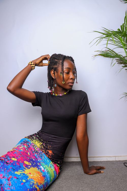 Free Woman elegantly posing in a black blouse and colorful skirt with vibrant patterns, seated against a plain background. Stock Photo