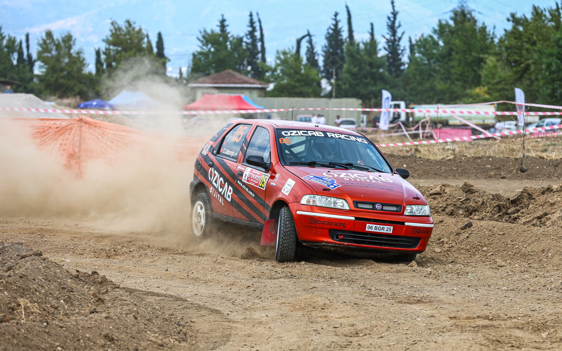 Fiat Palio rally car speeding through a dusty track during a rally event outdoors.