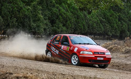 Free A red rally car kicks up dust while drifting through a forest track during a rally event. Stock Photo
