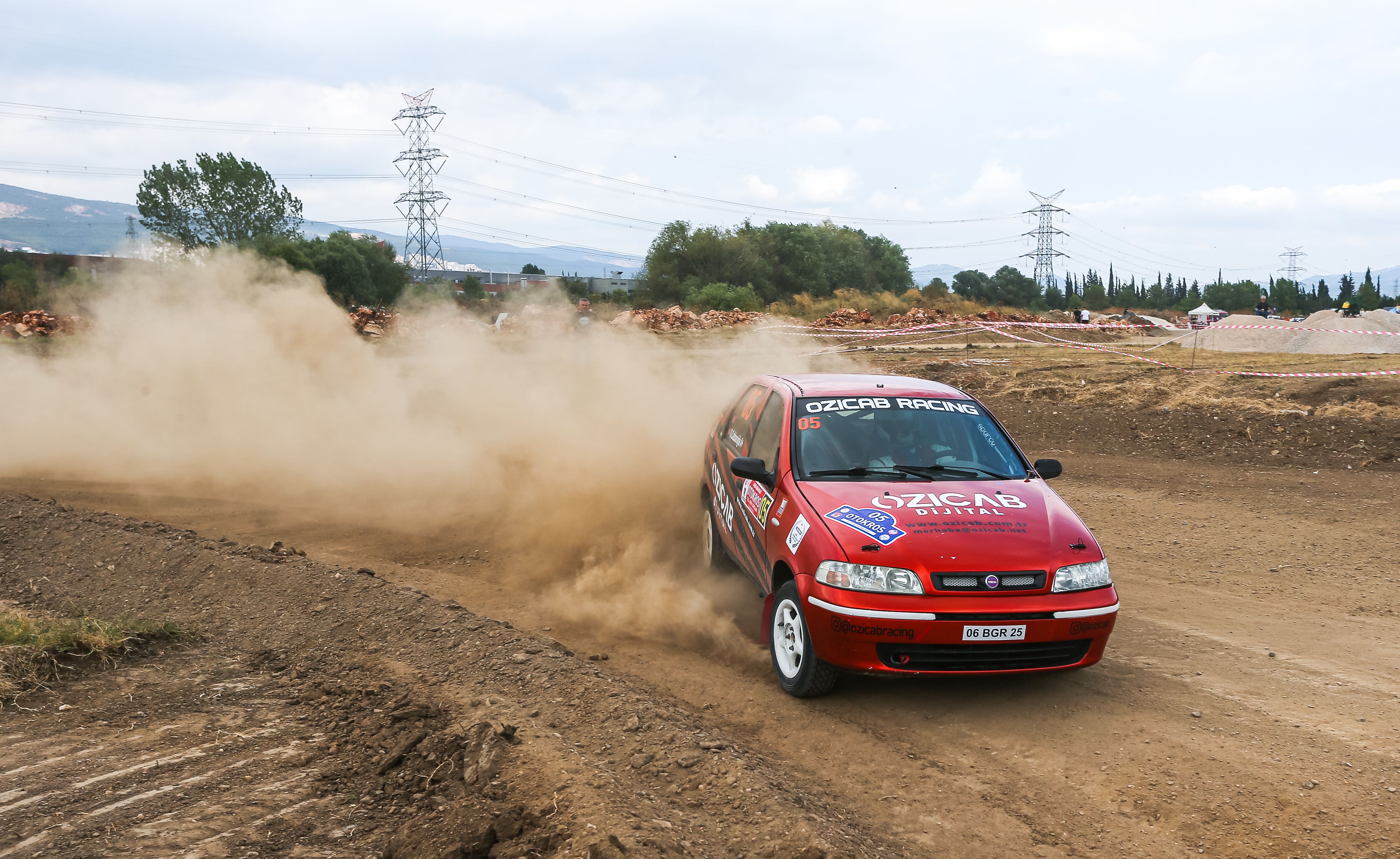 Red Fiat Palio car participating in a vibrant rallycross race on a dusty track.