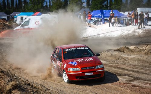 Free A red rally car speeds on a dirt track, creating a dramatic dust cloud with spectators watching. Stock Photo