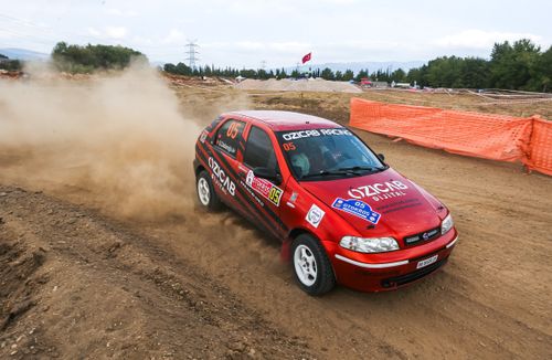 Free Red Fiat Palio racing on a dirt track during an exciting off-road rally event, creating impressive dust clouds. Stock Photo