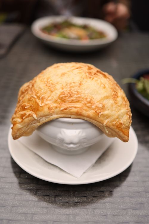 Free A delicious golden puff pastry covering a soup bowl on a table setting. Stock Photo