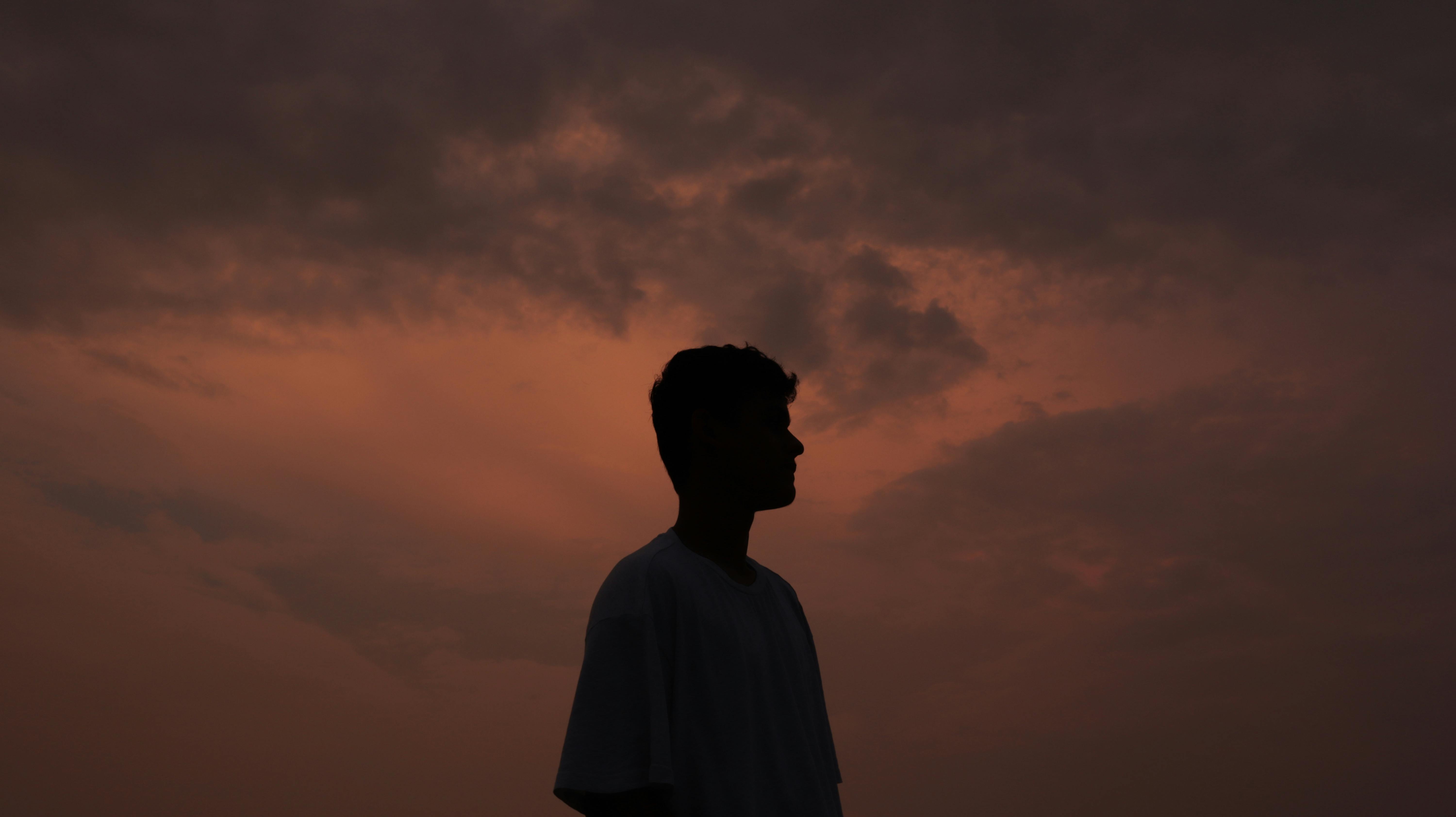 A dramatic silhouette of a man against a sunset sky, capturing a serene evening moment.