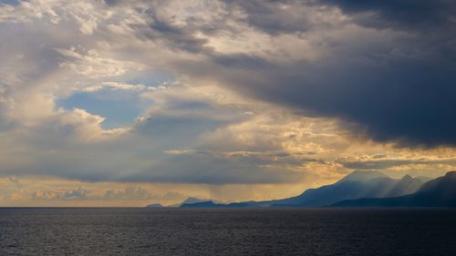 Free Breathtaking view of mountains, ocean, and dramatic sky at sunset. Stock Photo
