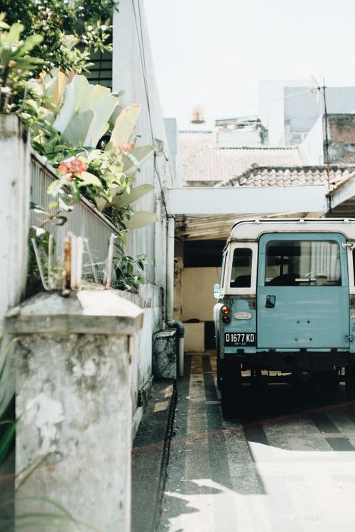 Free A classic blue Land Rover parked in a narrow urban alley beside a fence and flowers. Stock Photo