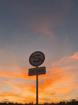Silhouette of a no parking sign against a vibrant sunrise sky with orange and blue hues.
