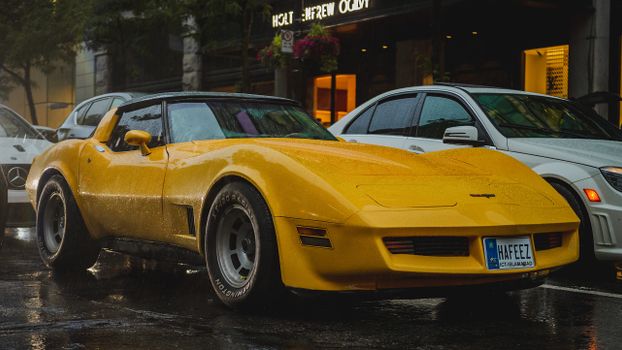 Captivating shot of a yellow Corvette parked on a rainy urban street.