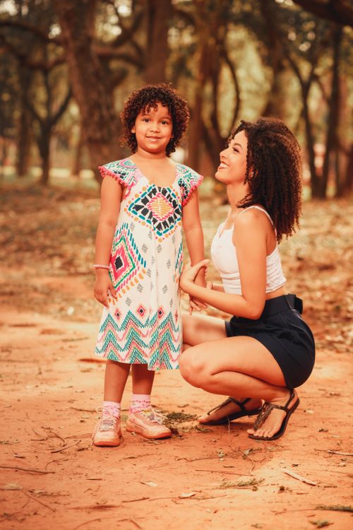Free A mother crouches, smiling at her daughter in a colorful dress during a warm autumn day in the park. Stock Photo