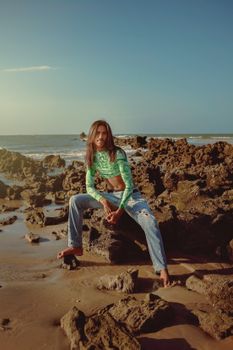 A woman sitting on rocks by the sea, enjoying the summer sun on a beautiful beach.