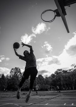 Teenager jumps to score on an outdoor basketball court in a dynamic black and white action shot.