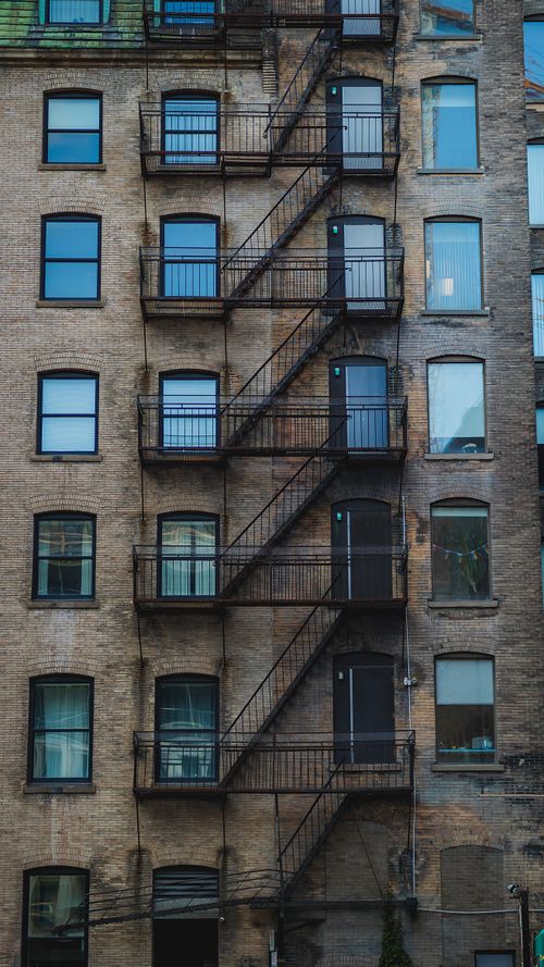 Free A textured brick building featuring classic fire escape stairs on a city street. Stock Photo