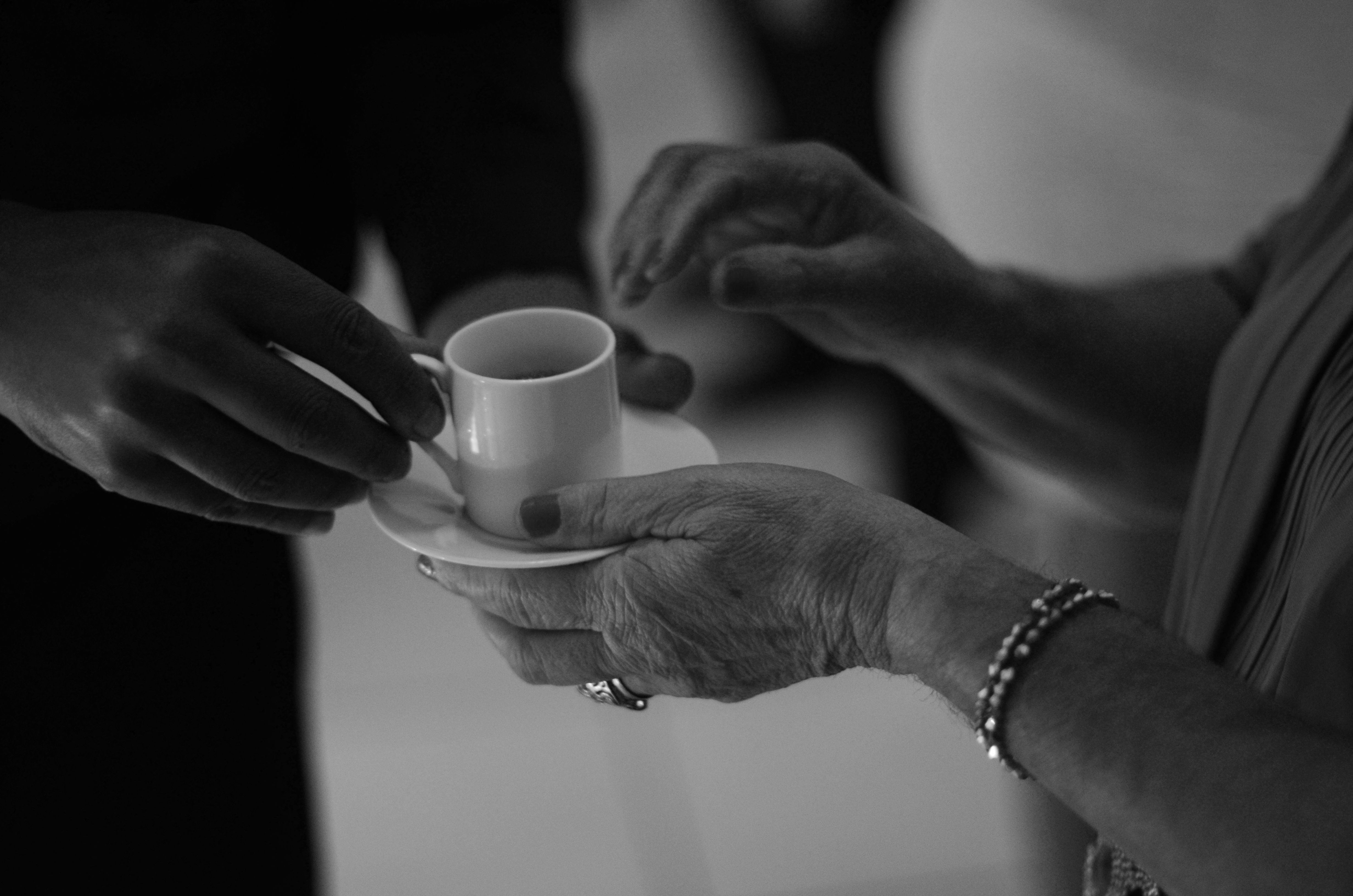 Close-up of hands exchanging a small coffee cup in a serene black and white setting.