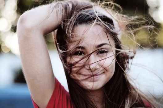 Cheerful girl with flowing brown hair enjoying a breezy day outdoors and smiling at the camera.