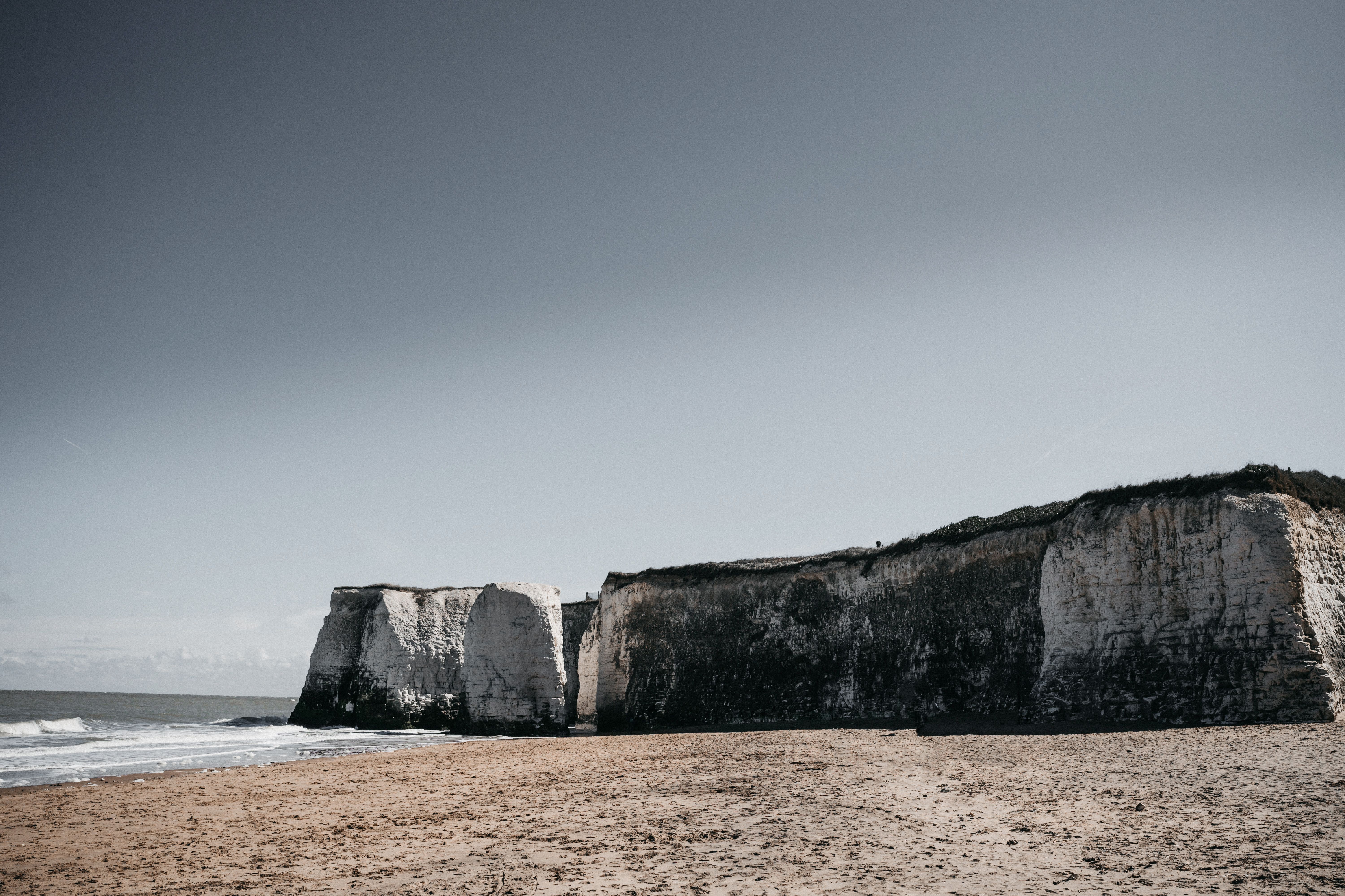 Majestic chalk cliffs overlooking a serene sandy beach on a clear day in Kent, England.