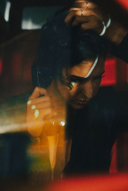 A moody and artistic portrait of a woman holding a phone, captured through a reflective surface with warm tones.