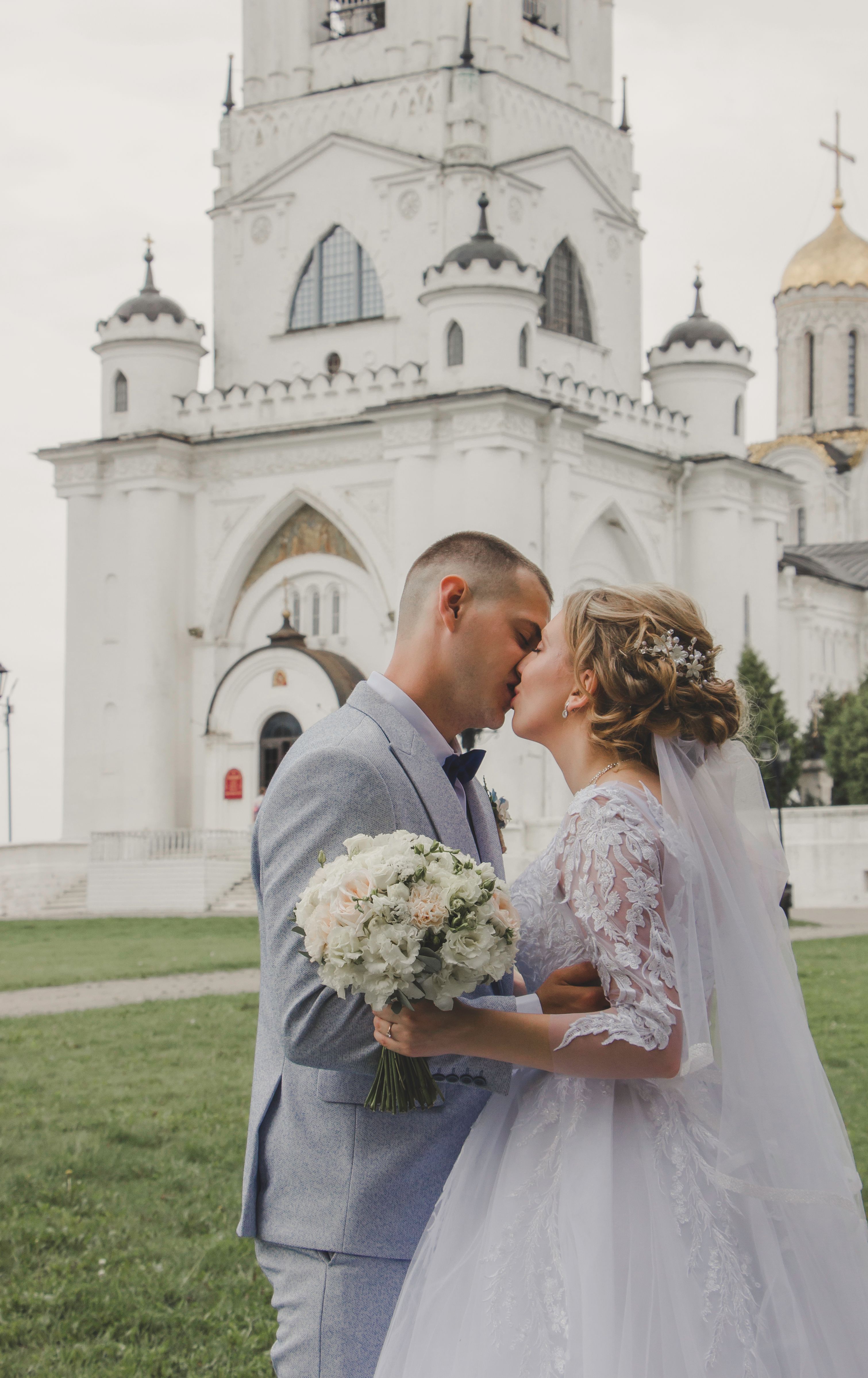 Bride and groom share a romantic kiss outdoors by a historic church.