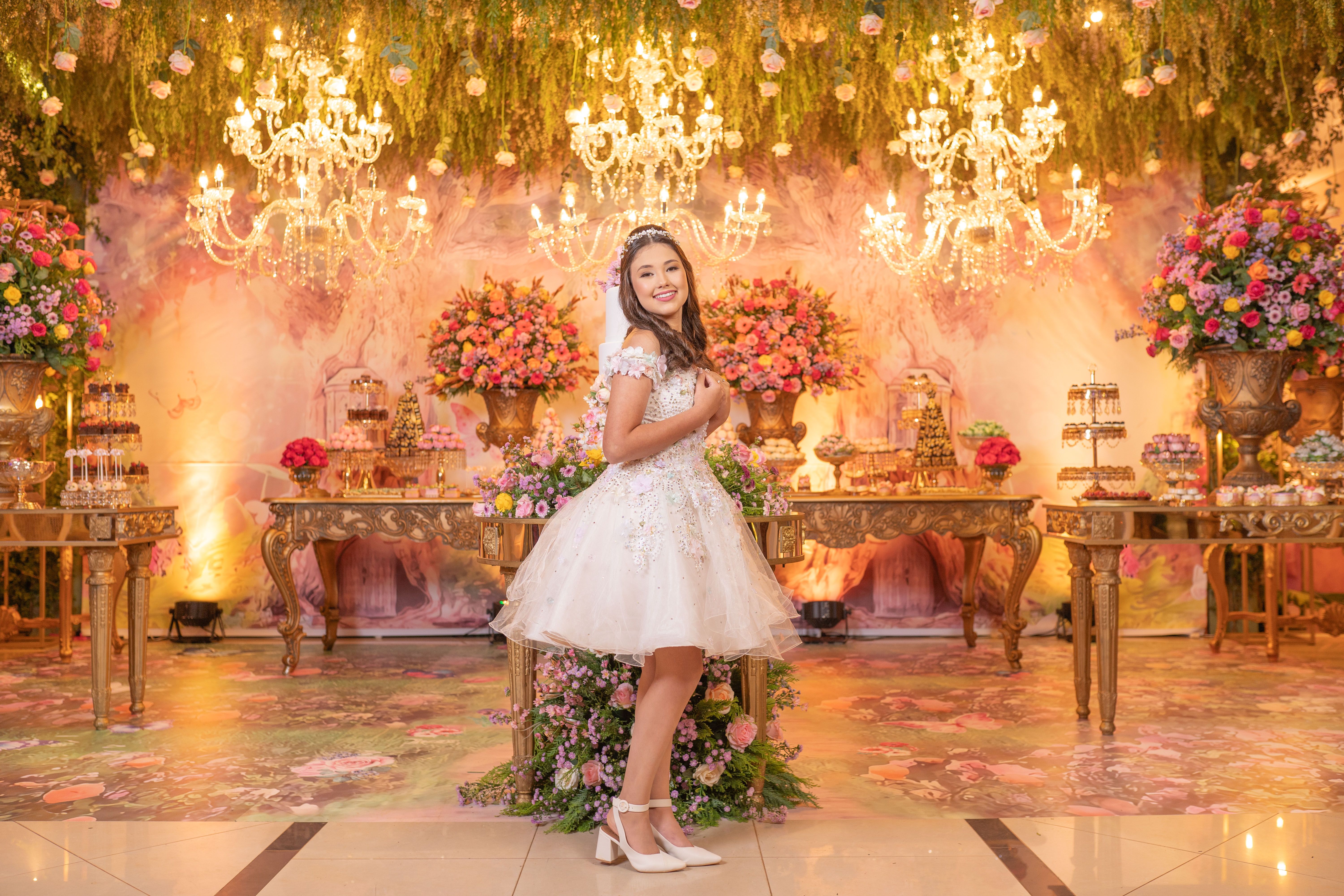 A joyful teenage girl at a quinceañera party with stunning floral decorations and chandeliers.