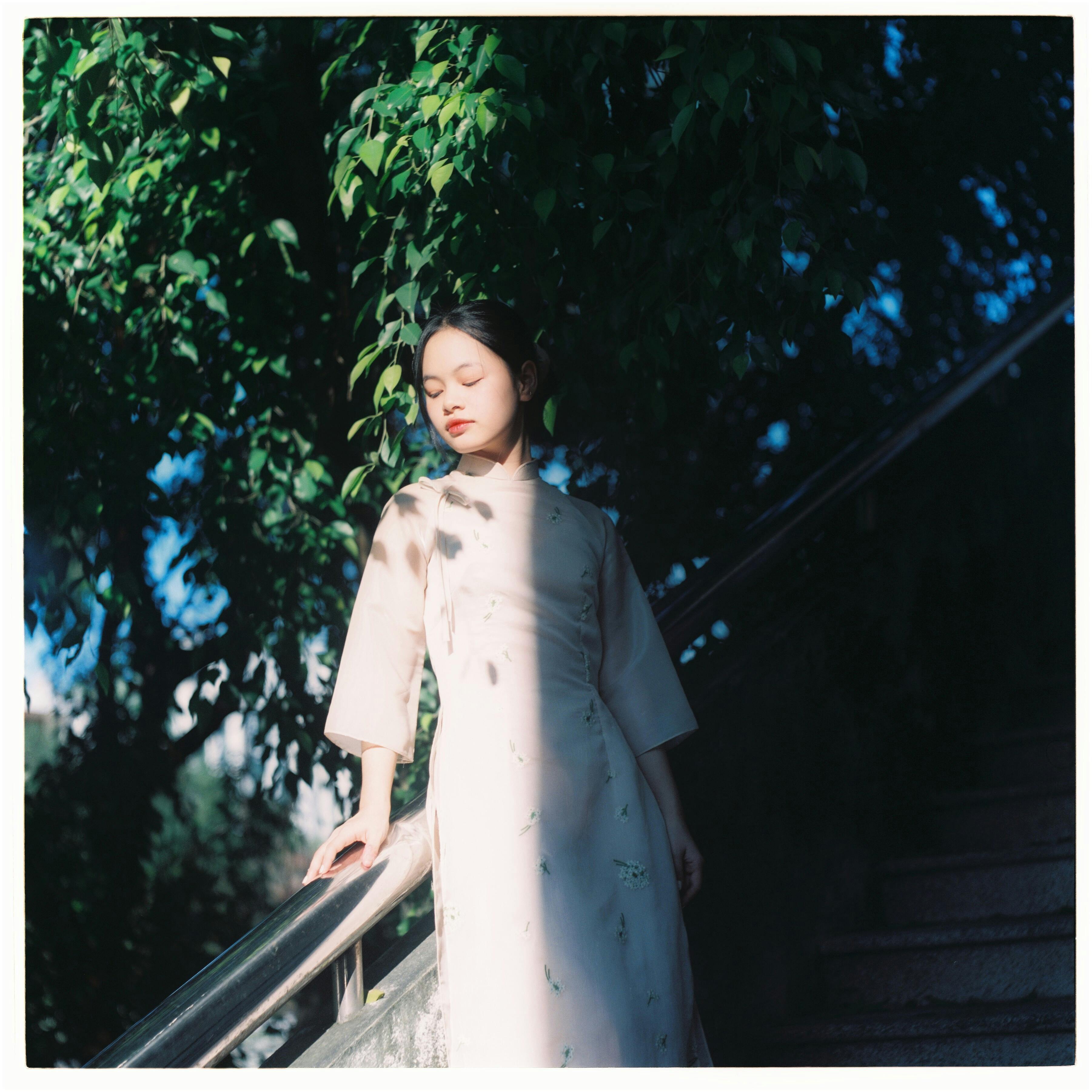 Elegant portrait of a woman in traditional dress with eyes closed, amidst natural surroundings.