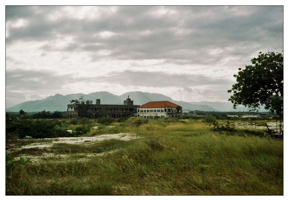 A scenic view of historical buildings in Cam Ranh, Vietnam, surrounded by grassland and mountains.