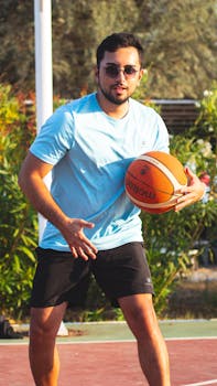 Adult male playing basketball on an outdoor court in the sun.