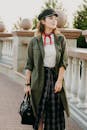 一位穿着绿色夹克和格子裙的时尚女子在户外背着黑色包摆姿势