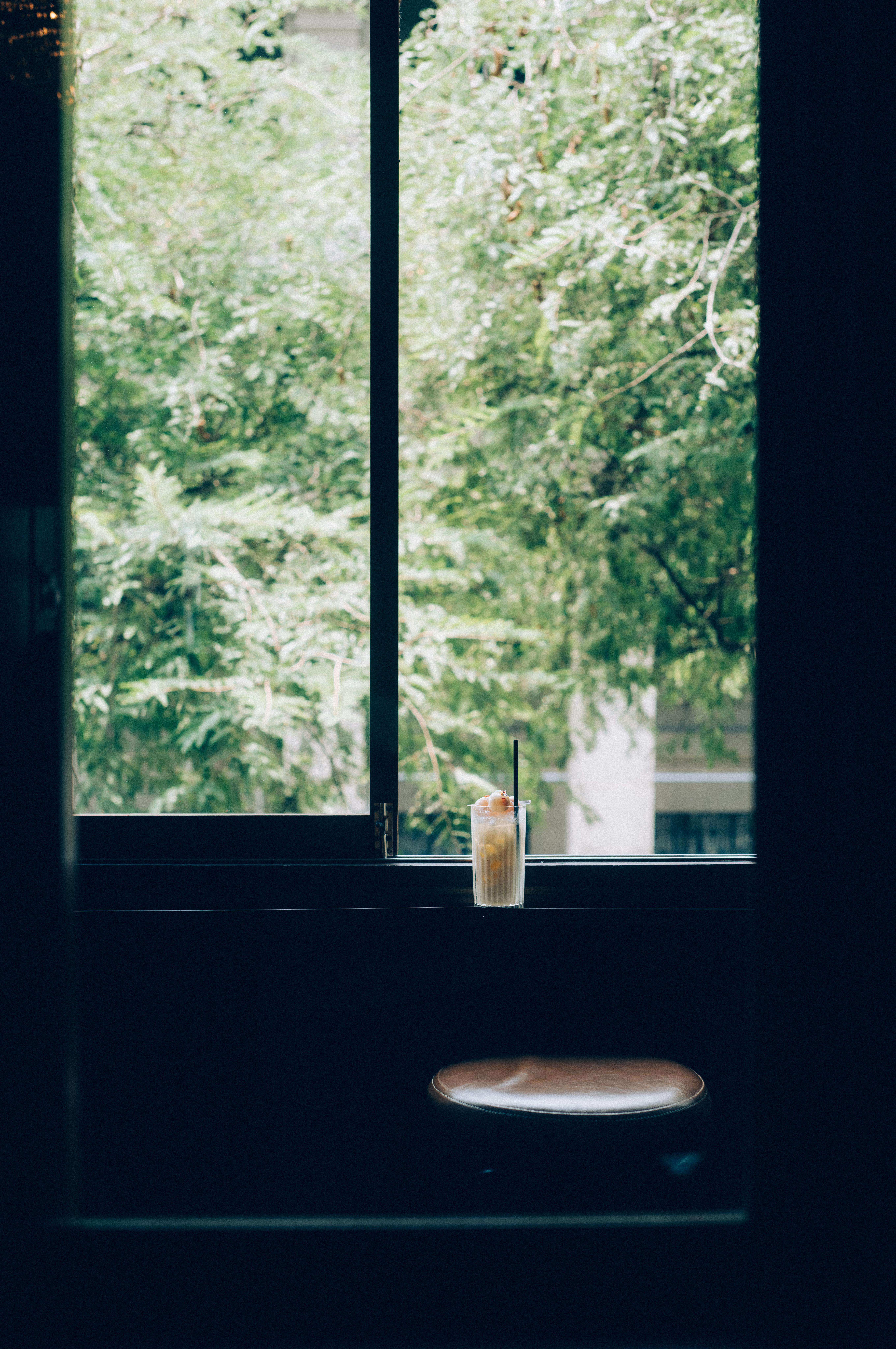 A refreshing cocktail on a window ledge, capturing tranquility with a lush tree view outside.
