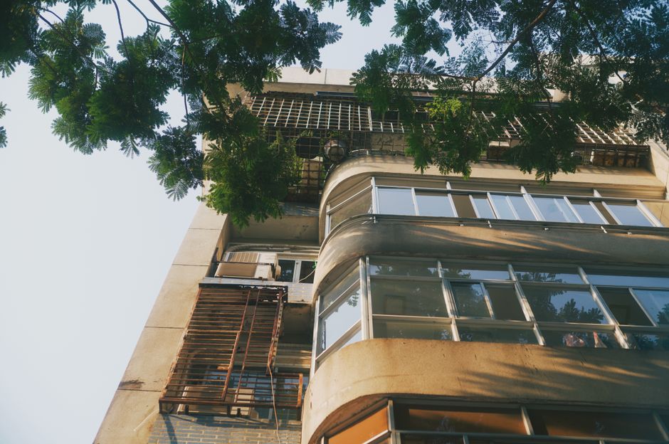 Low angle view of a residential building facade with lush green foliage in an urban setting.
