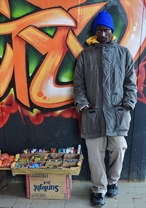 A Man Standing near a Wall with Graffiti and Selling Items 