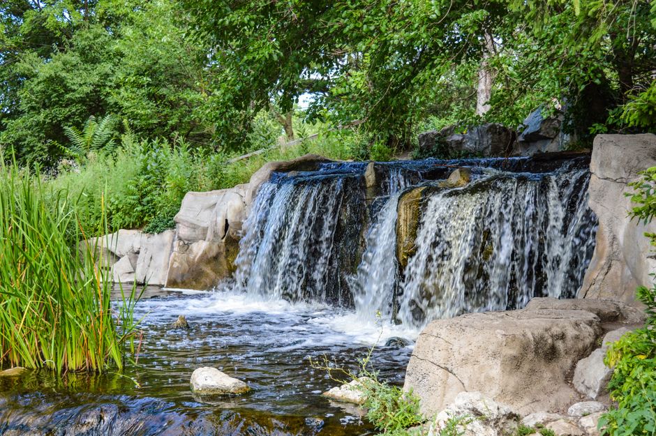 A picturesque waterfall flows through lush greenery in a serene park setting.