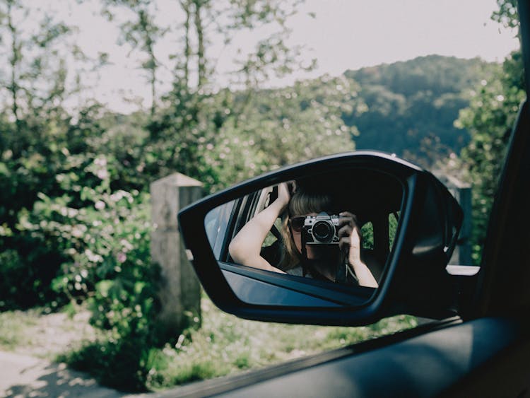 A Woman Taking A Photo Reflecting In A Rear-View Mirror