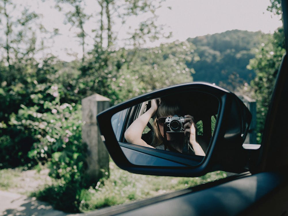A woman taking a photo reflecting in a rear view mirror
