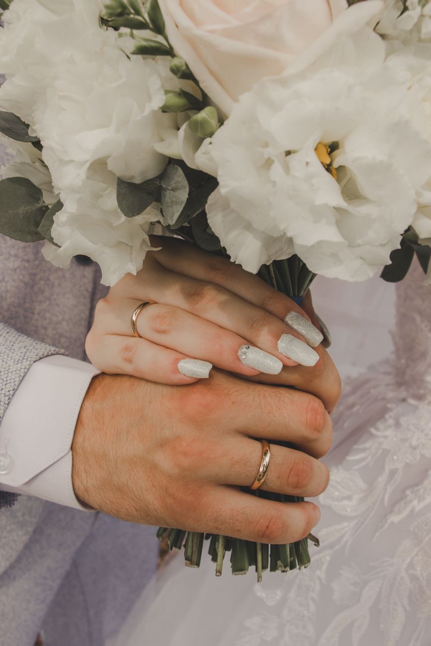 Close-up image of bride and groom's hands holding a bouquet, symbolizing love and commitment.