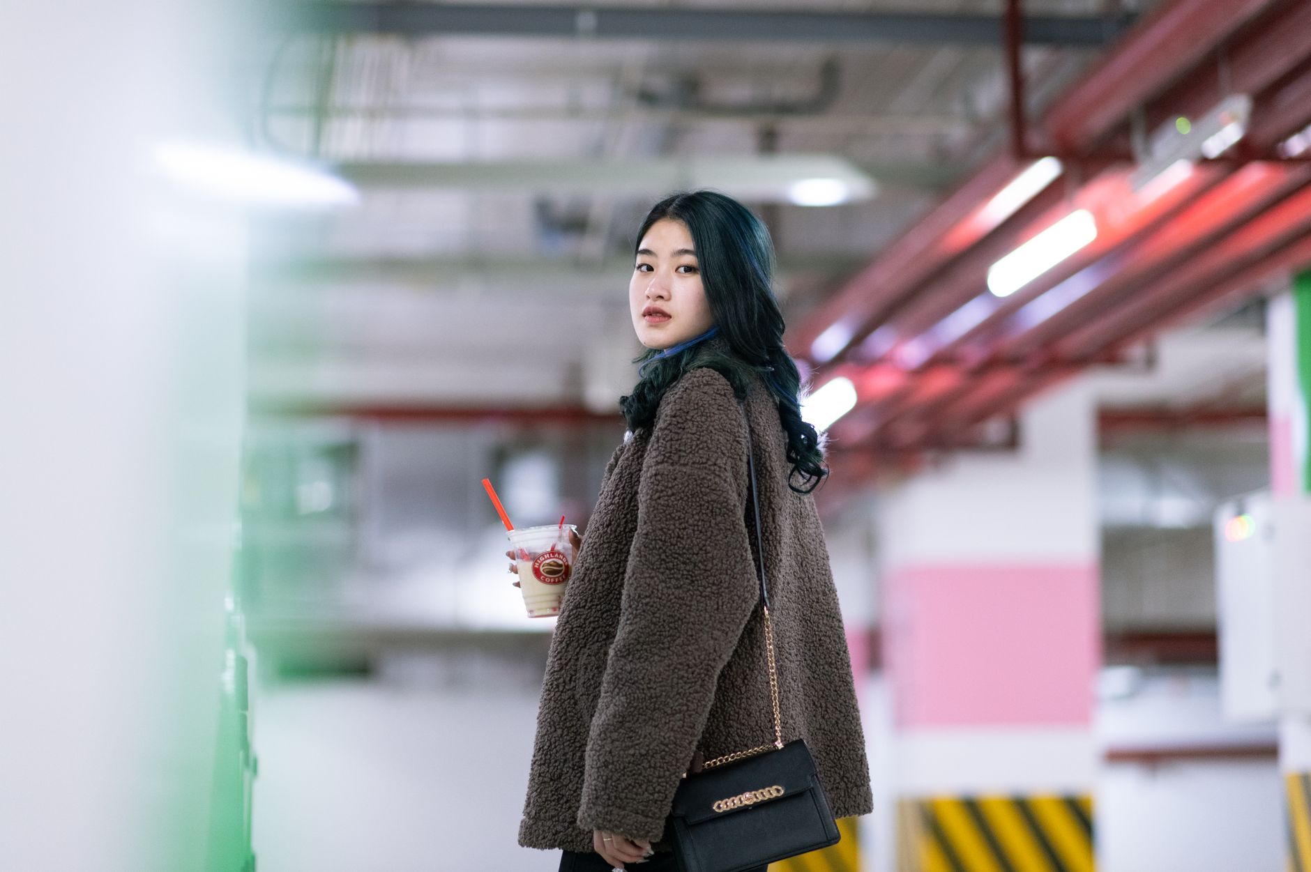 Woman with drink in an urban parking lot wearing a cozy jacket.